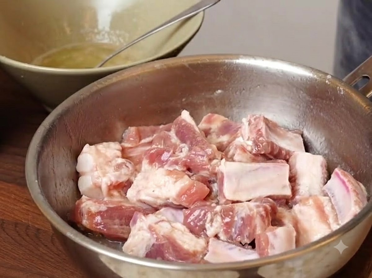 Morceaux de côtes de porc dans un bol en métal avec des assaisonnements et des fécules ajoutés avant le mélange.
