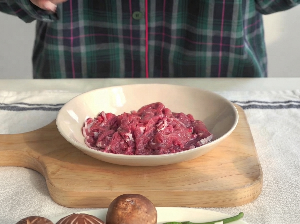 Morceaux de filet de bœuf dans un bol peu profond en train dêtre marinés avec de la sauce huître et de la fécule de maïs.
