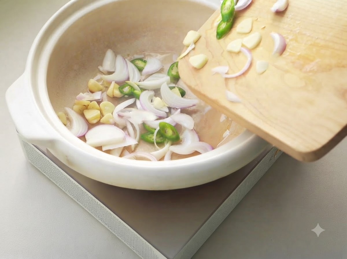 Oignons émincés, ail et piments en train de grésiller dans une casserole en céramique blanche.
