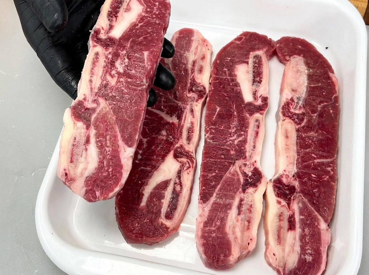 Une main gantée tenant un travers de bœuf LA cru avec os, montrant son persillage riche et sa structure osseuse.