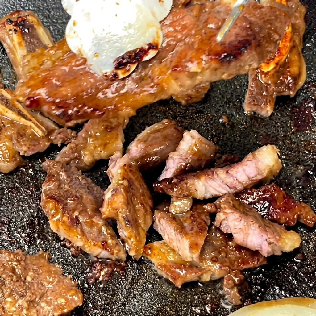 Des pinces tenant un travers de bœuf cuit pendant que des ciseaux le découpent en plus petites portions sur une poêle chaude.