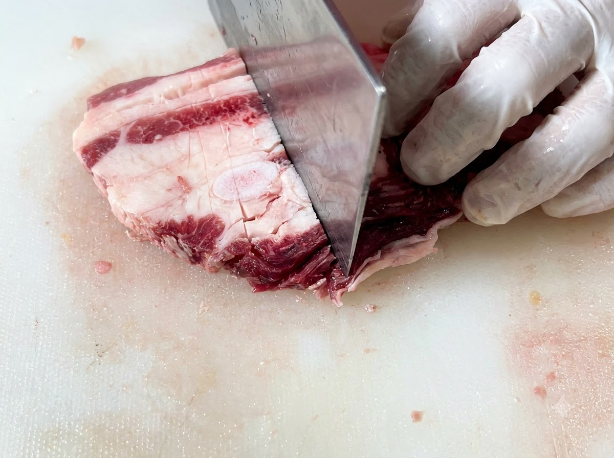 Côtes de bœuf crues en train dêtre tranchées en morceaux rectangulaires uniformes sur une planche à découper à laide dun grand couteau.