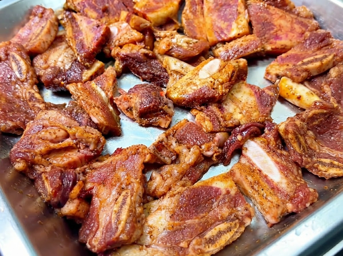 Côtes de bœuf marinées disposées dans un plateau métallique avec des oignons émincés saupoudrés sur le dessus.