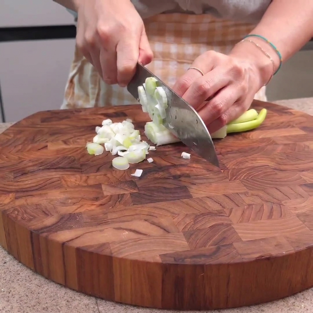 Oignons verts hachés sur une planche à découper en bois avec un couteau de chef.
