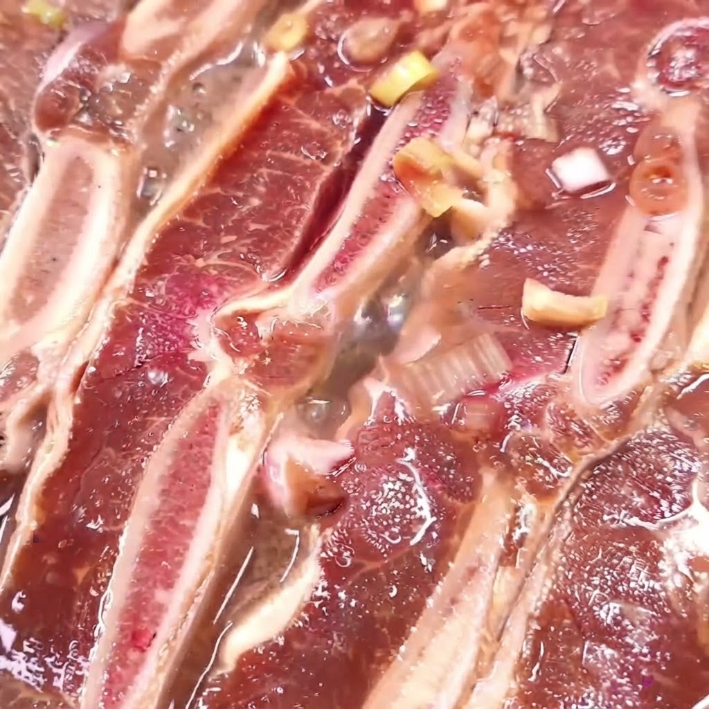 Côtes de bœuf cuisant dans une poêle avec une marinade bouillante en train de réduire.