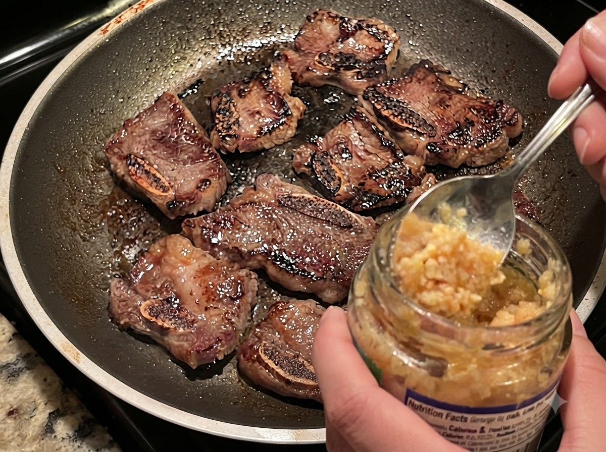 De lail émincé prélevé dun pot à la cuillère dans une poêle chaude avec des côtes de bœuf dorées et des oignons.