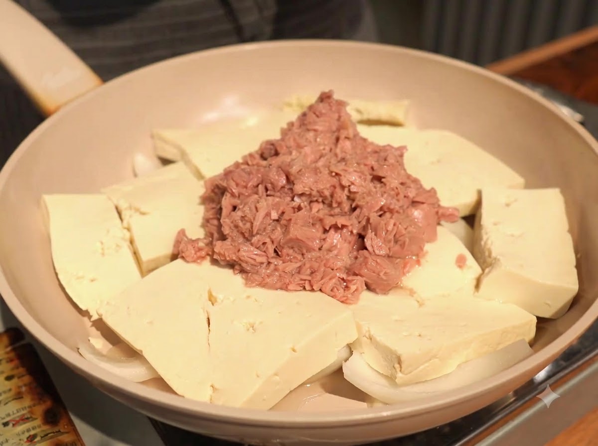 Ail haché ajouté dans la poêle, déposé sur le tofu à côté du thon.