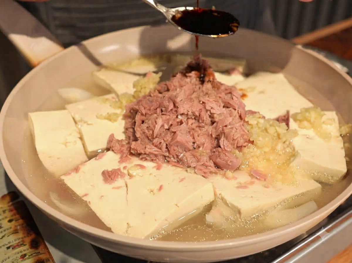 Sauce soja versée à la cuillère sur le thon en conserve et les morceaux de tofu.