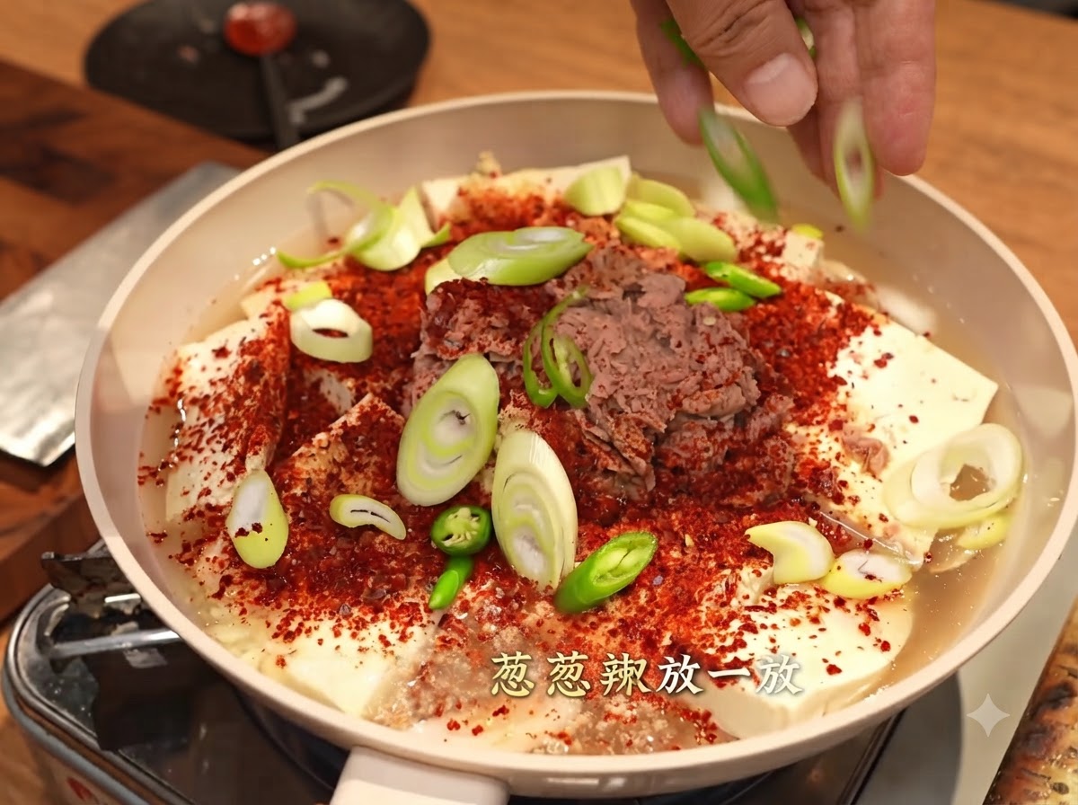 Mains parsemant de la ciboule et des piments verts tranchés sur le plat couvert de flocons de piment rouge.