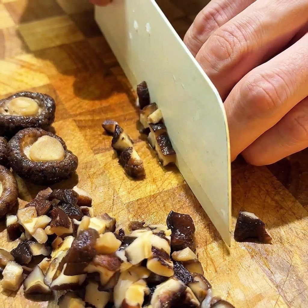 Des champignons shiitake réhydratés coupés en petits cubes avec un couteau blanc sur une planche en bois.