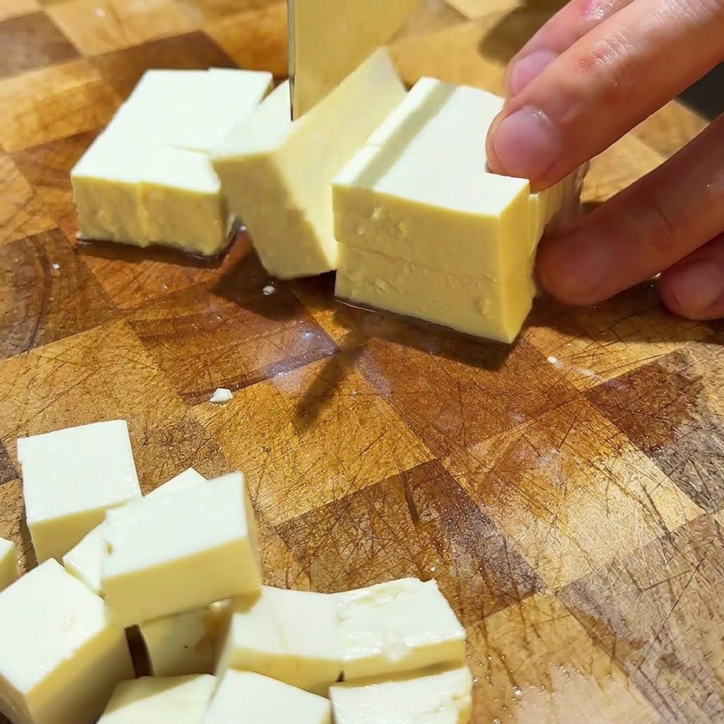 Du tofu soyeux coupé en petits cubes réguliers sur une surface de découpe en bois.
