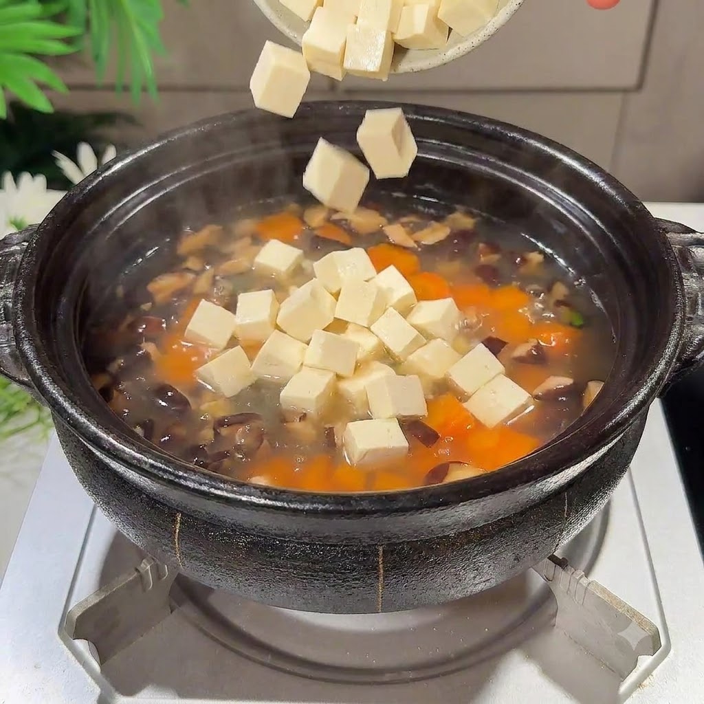 Des morceaux de tofu soyeux en dés tombant dans le pot de soupe frémissante.
