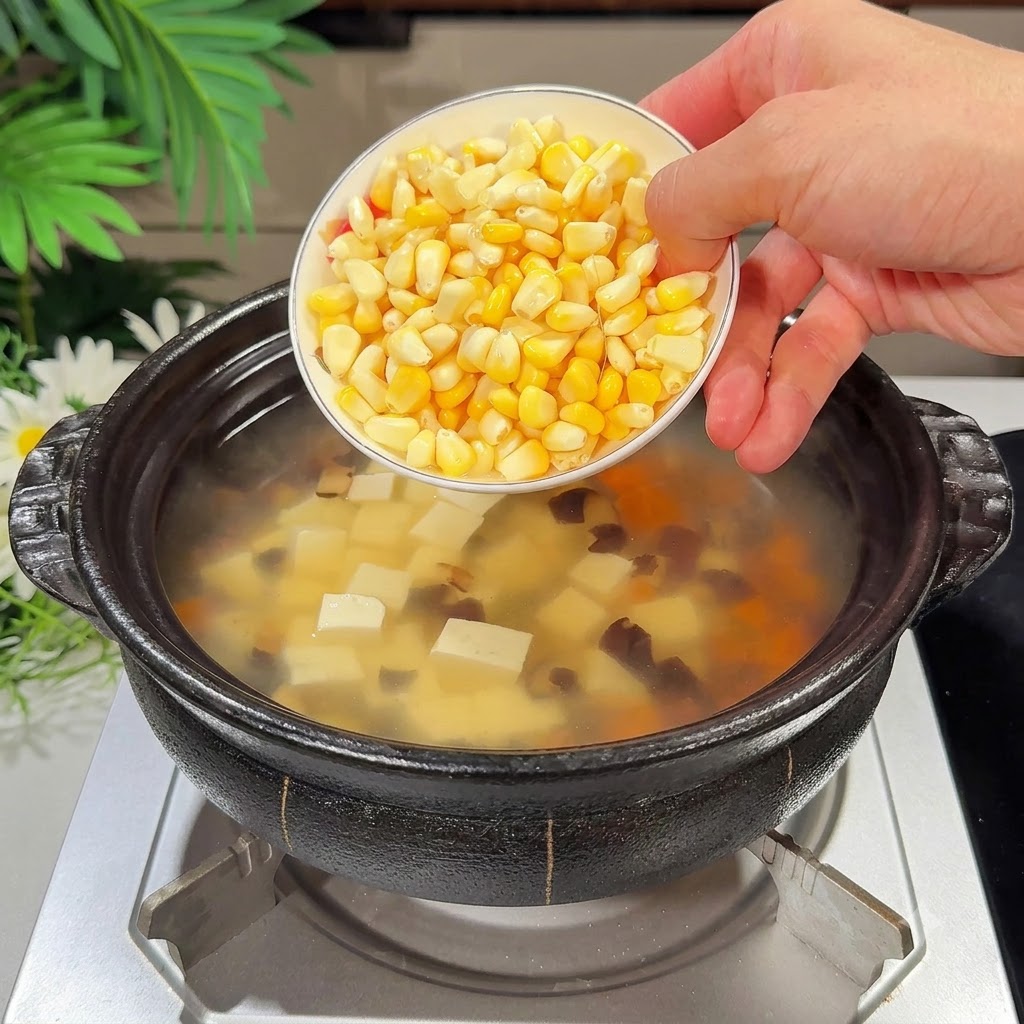 Un petit bol de grains de maïs frais versés dans le pot de soupe.