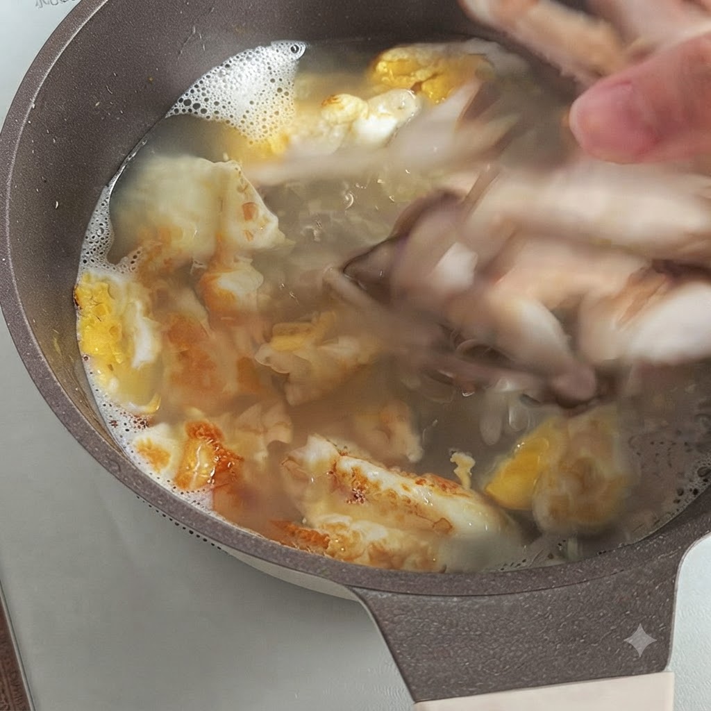 Une main ajoutant des champignons shiitakes frais émincés dans un bouillon bouillonnant avec des morceaux dœufs frits.