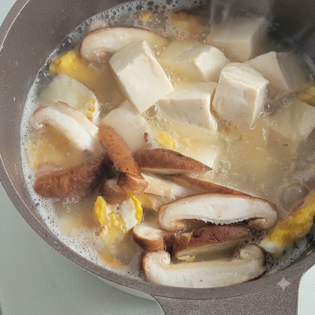 Cubes de tofu blanc tendre mijotant dans un bouillon savoureux aux côtés de champignons émincés et de morceaux dœufs frits.