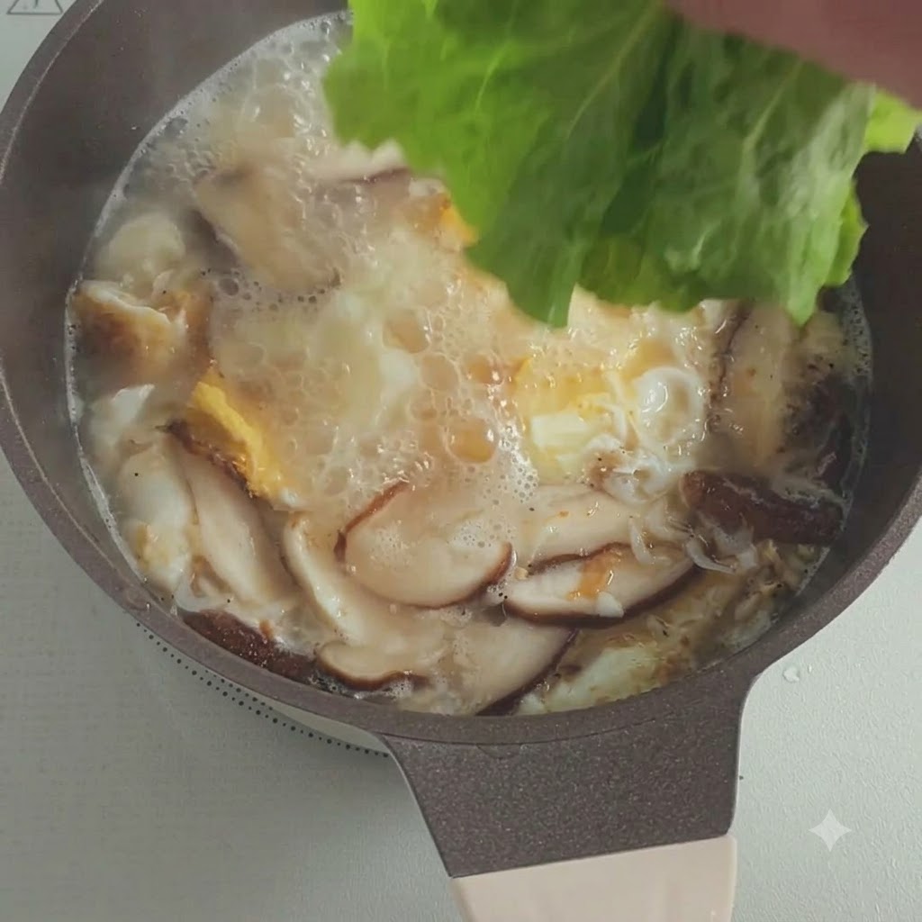 Des feuilles de laitue fraîche ajoutées dans une marmite de soupe frémissante avec des champignons et des œufs.