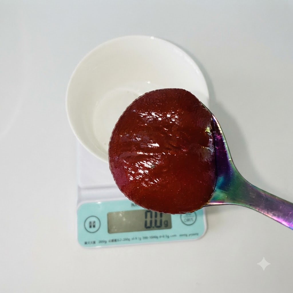 Une cuillère de pâte de piment coréenne rouge tenue au-dessus dun bol blanc reposant sur une balance de cuisine numérique.