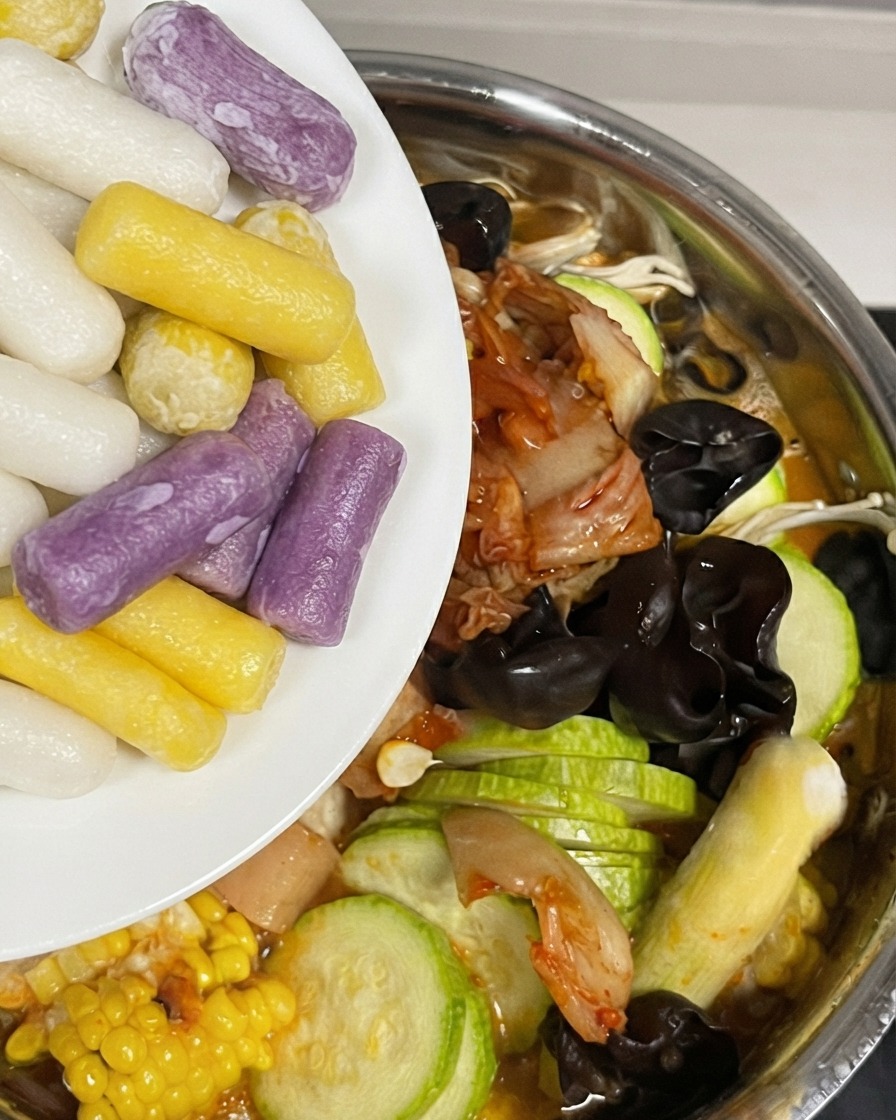 Ajout de gâteaux de riz au fromage colorés dans la marmite remplie dingrédients et de sauce.