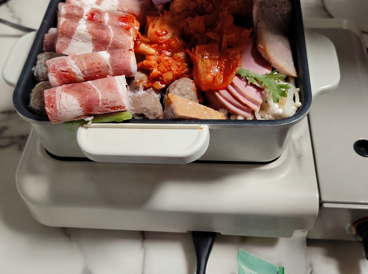 Un plat chaud rempli de couches de viande, de légumes et de galettes de riz avec du bouillon versé par-dessus.