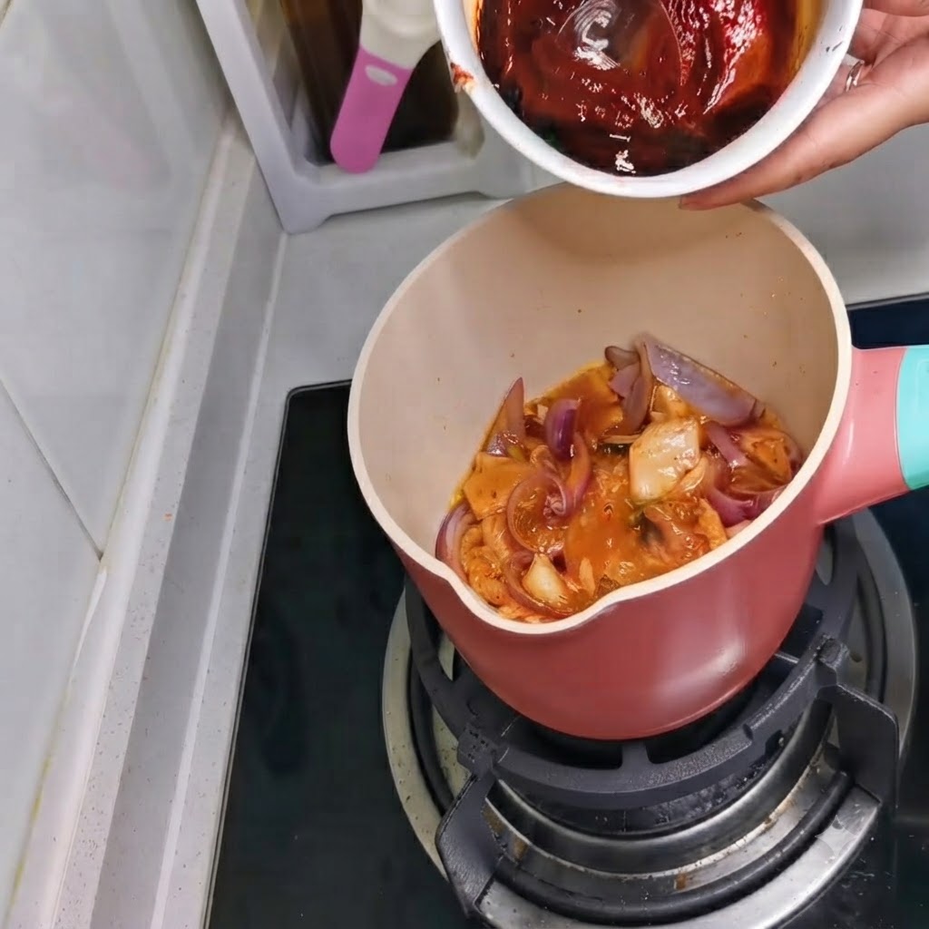 Un bol contenant un mélange de sauce rouge foncé versé dans la casserole.