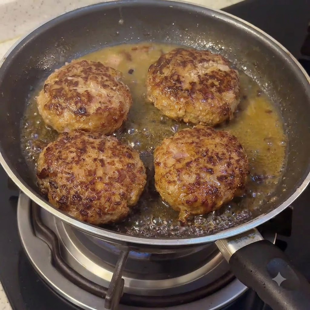 Un bloc de beurre et des composants de sauce en train de fondre dans la poêle avec les steaks hachés grésillants.
