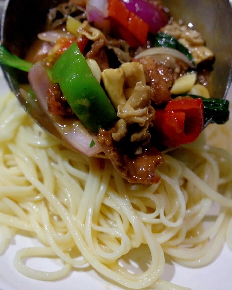 Une louche versant un mélange chaud sauté de champignons, de viande et de poivrons sur une assiette de nouilles nature cuites.