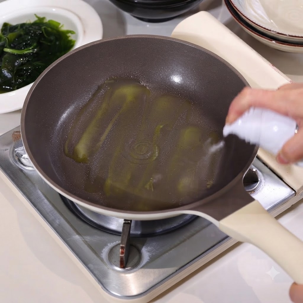 Une poêle antiadhésive recouverte dhuile de cuisson vaporisée à partir dun flacon blanc, avec un bol dalgues vertes à proximité.