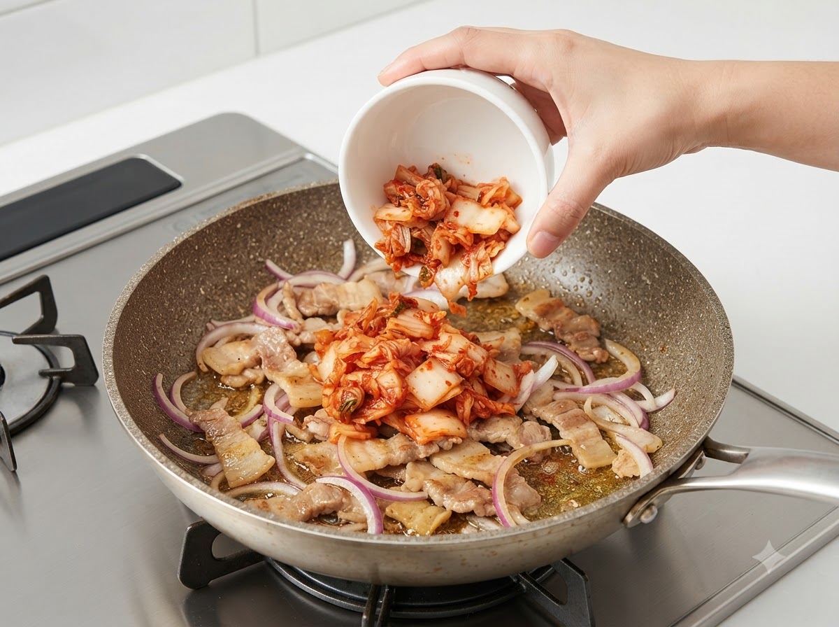 Un bol de kimchi haché versé dans la poêle grésillante avec le porc et les oignons.