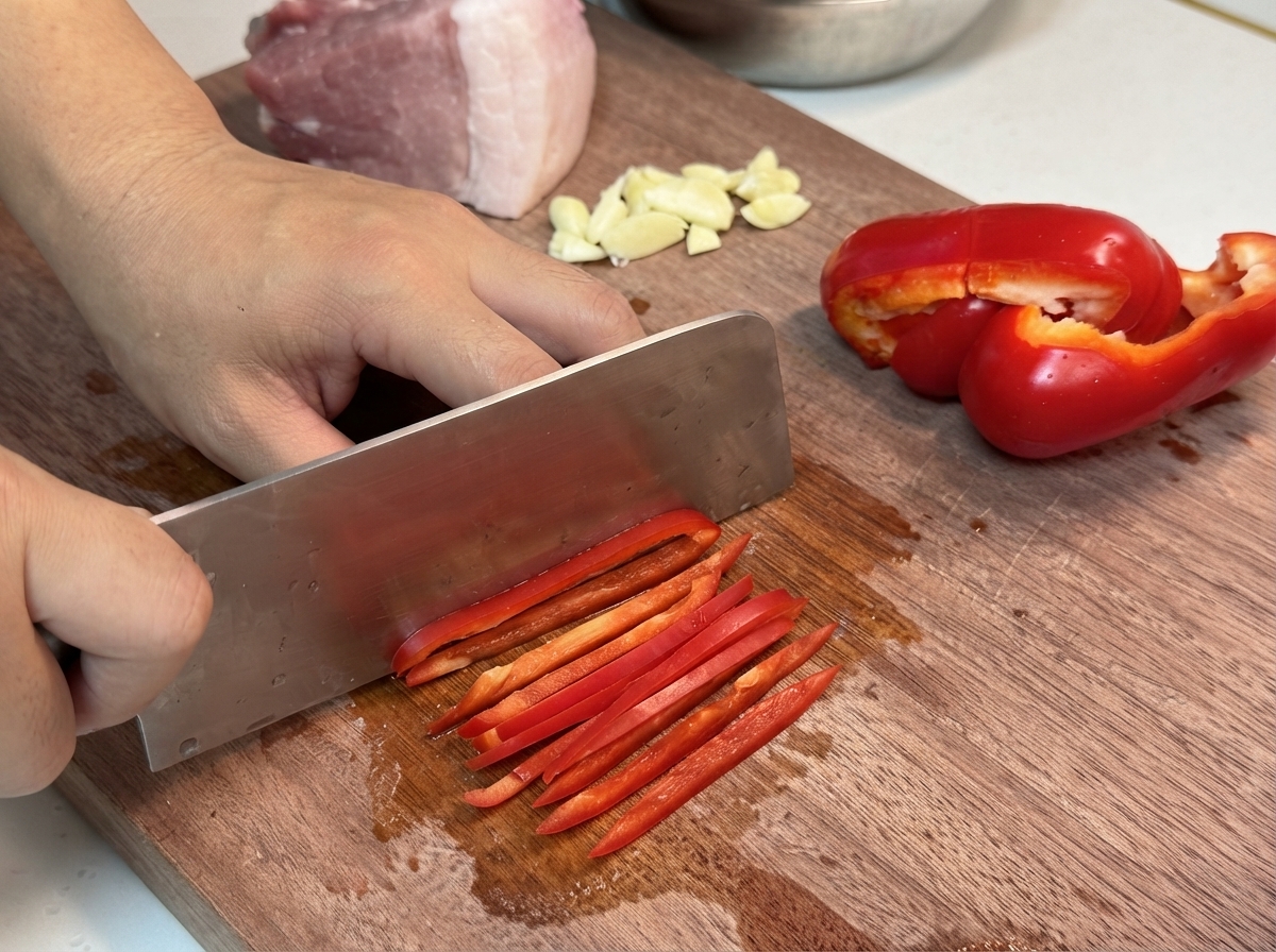 Poivrons rouges doux coupés soigneusement en de longs lanières régulières sur une planche en bois.