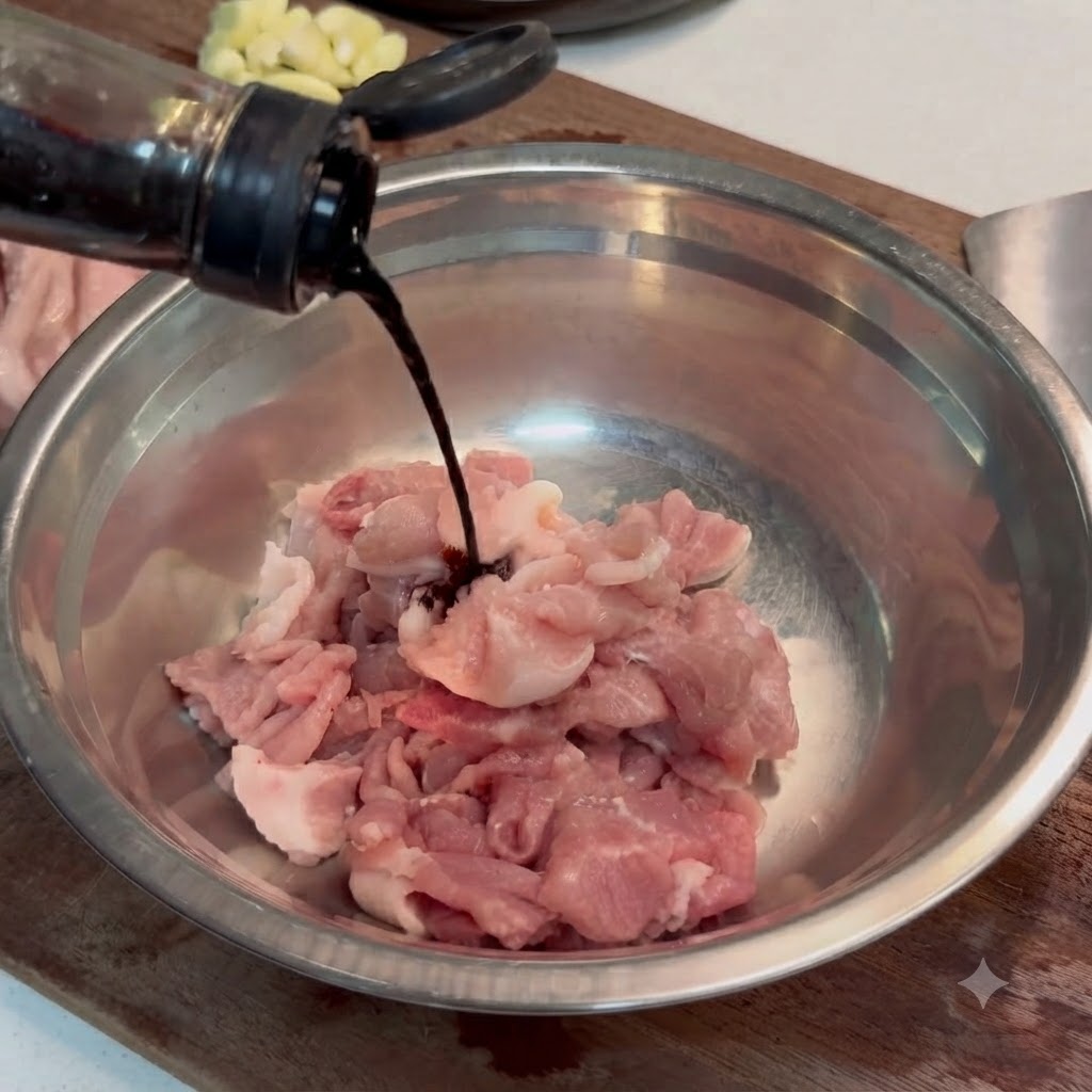 Sauce soja foncée et eau versées sur des tranches de porc cru dans un bol en métal.
