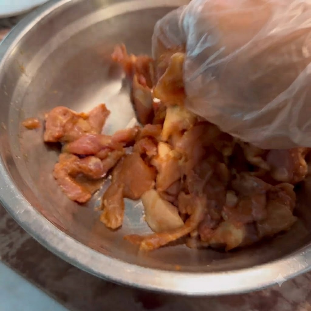 Une main gantée mélangeant les tranches de porc et la marinade dans un bol en métal.