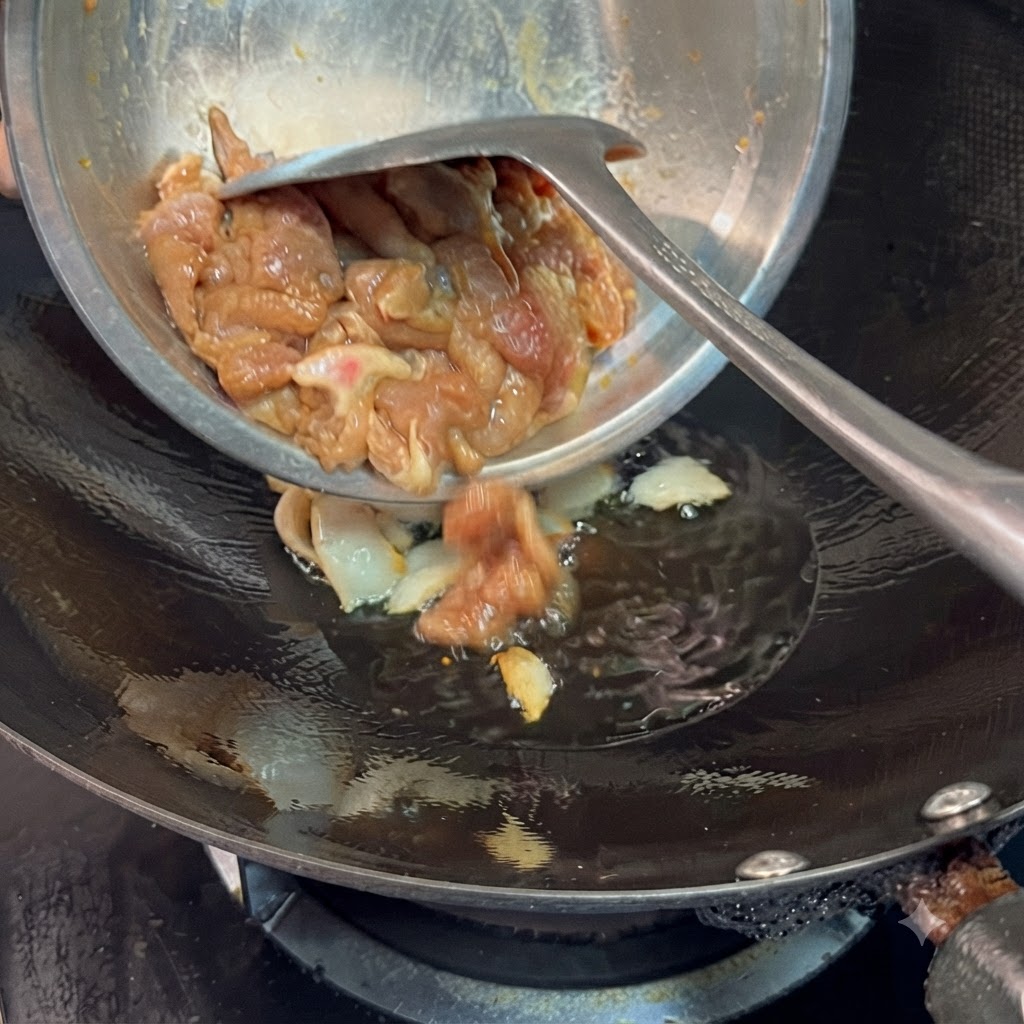 Tranches de porc marinées versées dun bol en métal dans un wok avec de lhuile et remuées avec une spatule.