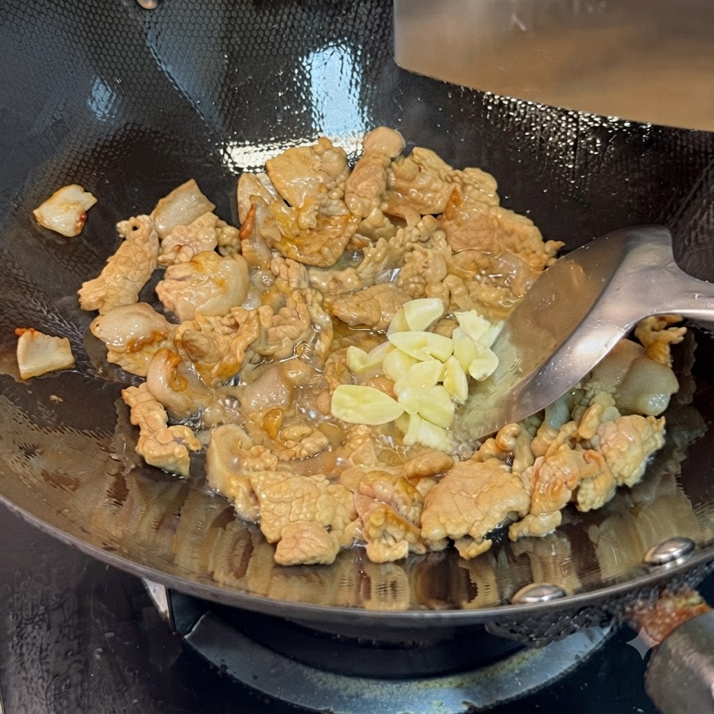 Ail émincé et pâte de soja ajoutés aux morceaux de porc cuits dans le wok.