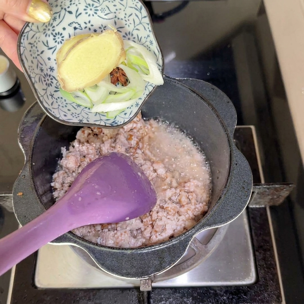Un petit bol contenant des tranches de gingembre, de lanis étoilé et des oignons nouveaux ajoutés dans la casserole.