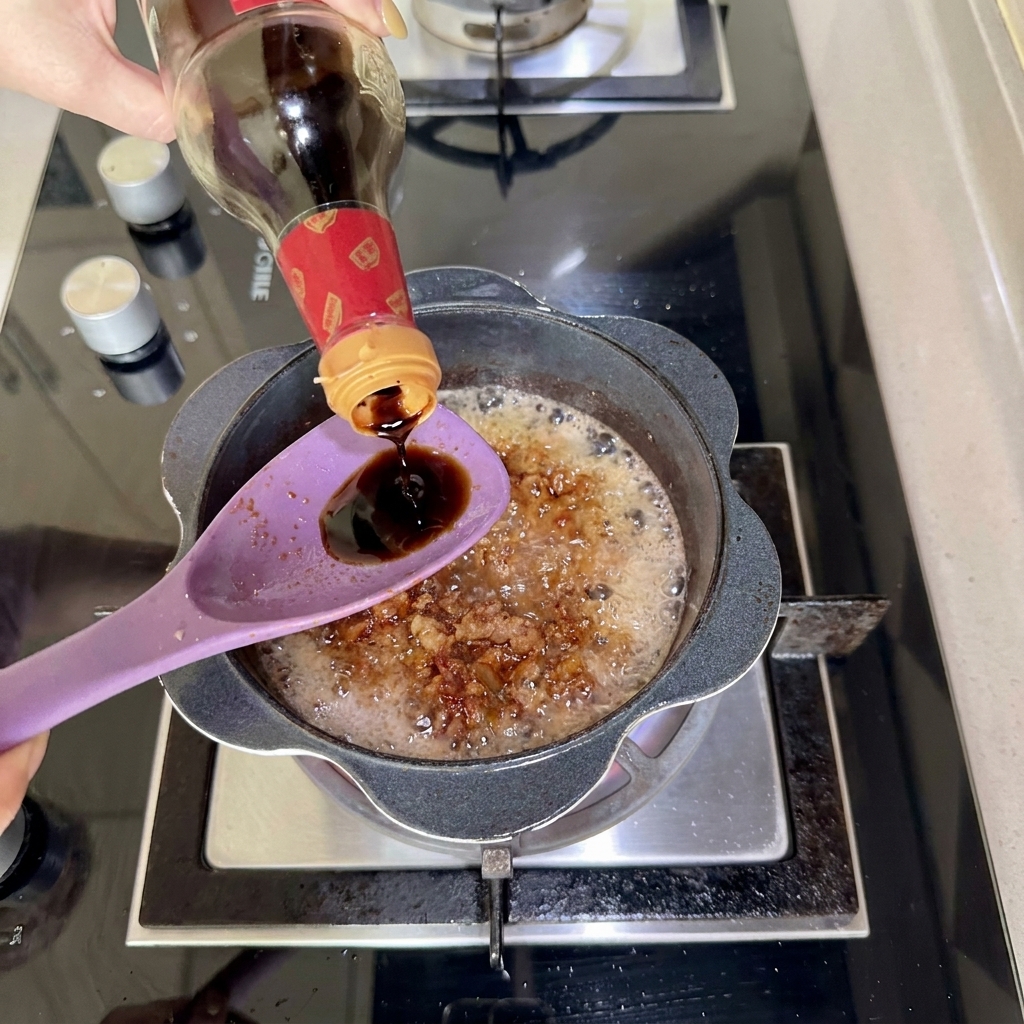 De la sauce soja noire versée dune bouteille sur une cuillère tenue au-dessus de la casserole.