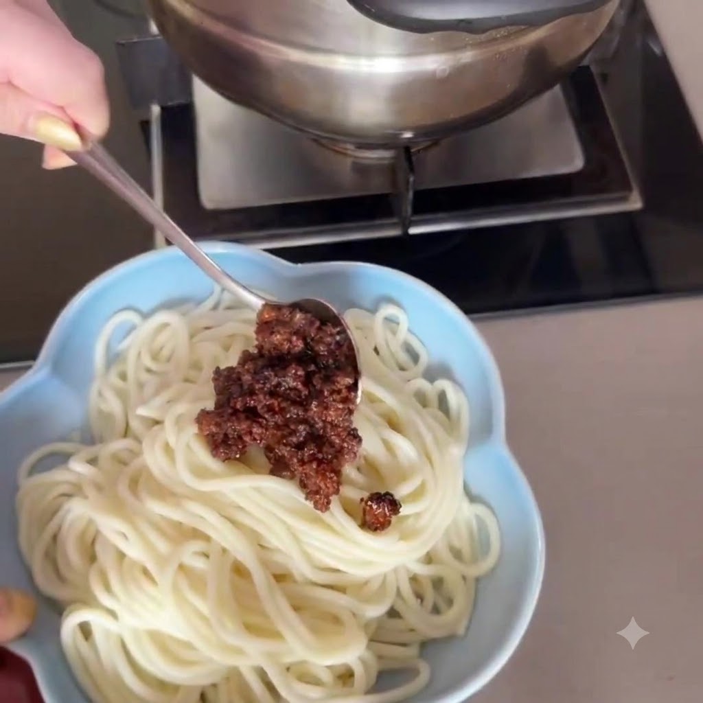 Vue rapprochée dune cuillère déposant délicatement une riche sauce de porc haché brun sur un bol de nouilles blanches.
