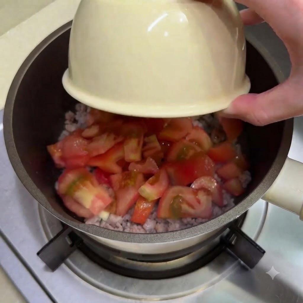 Des dés de tomates versés depuis un bol dans la casserole contenant le mélange de viande.
