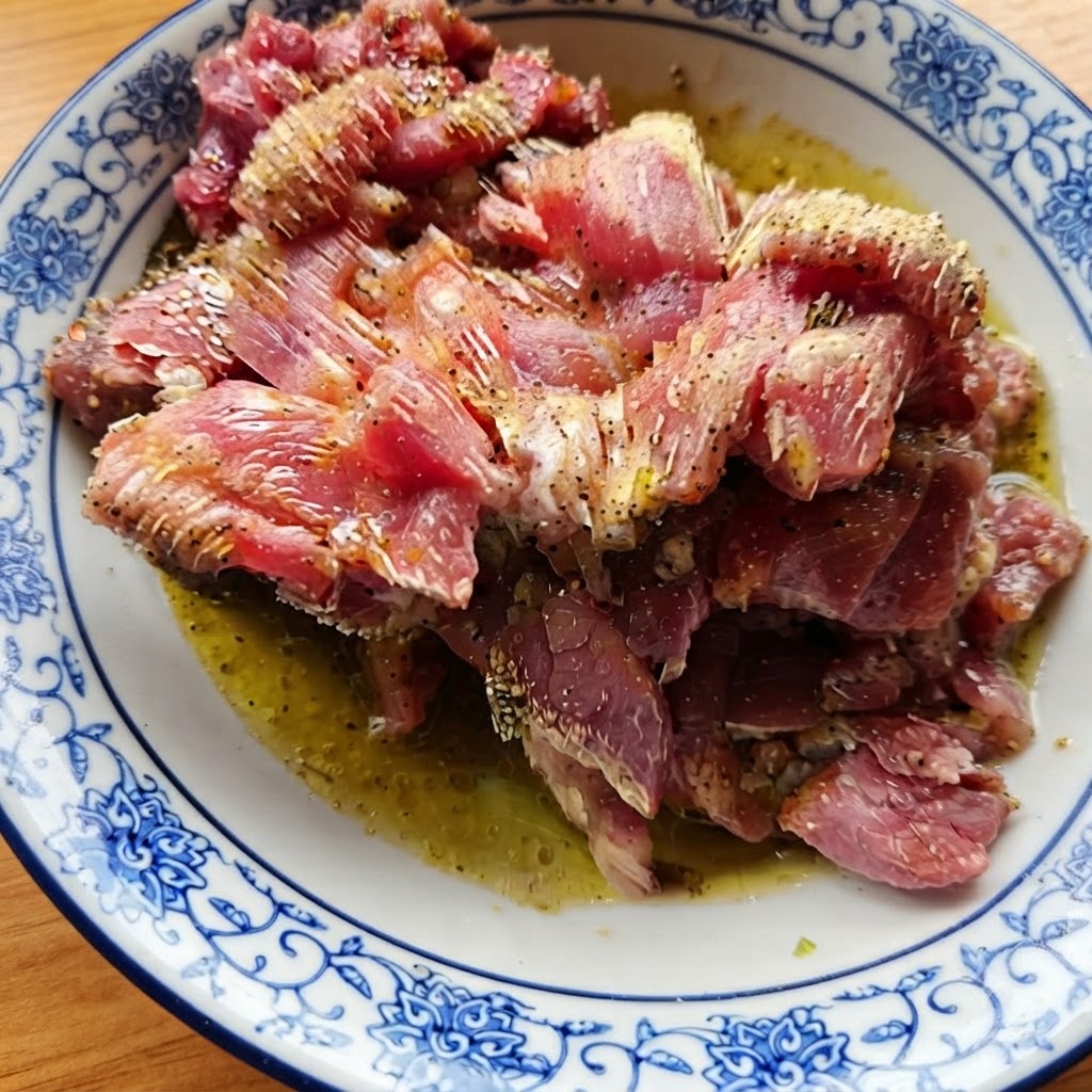 Morceaux de bœuf cru assaisonnés brillant dhuile et dépices dans un bol en céramique à motifs.