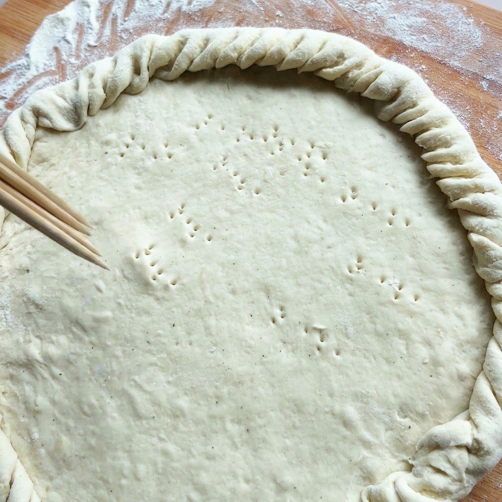 Des baguettes en bois perçant de petits petits trous dans une grande croûte de pâte circulaire avec un bord tordu.