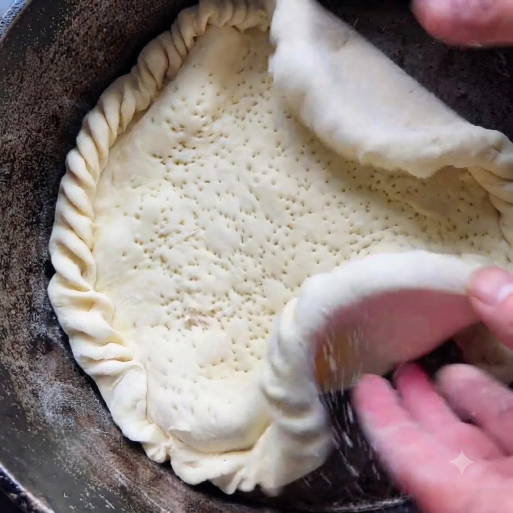 Des mains plaçant doucement une grande croûte de pâte avec des bords pliés dans un pot de cuisson sombre.