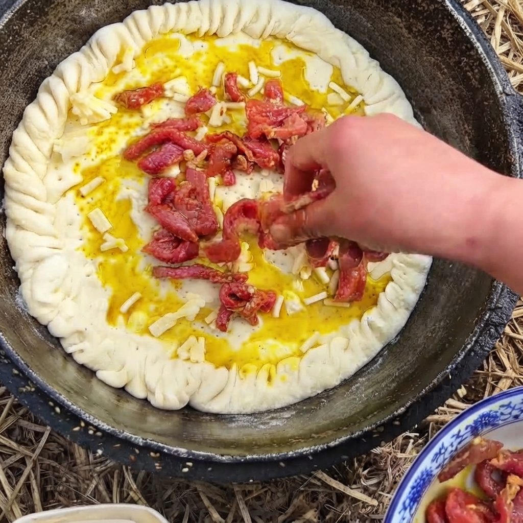 Une main plaçant des lanières de bœuf assaisonnées rougeâtres sur une base de pâte recouverte de fromage dans une poêle.