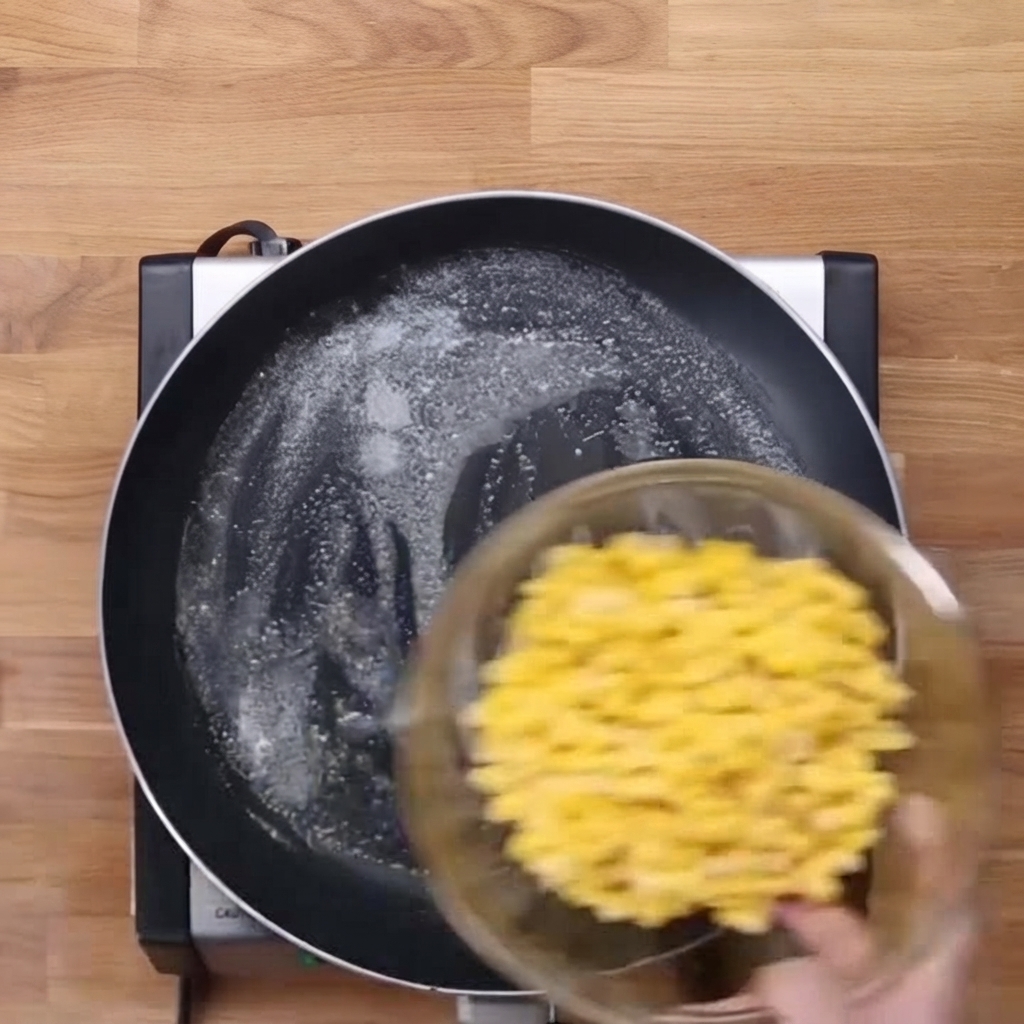Des grains de maïs jaune glissant dun bol en verre dans une poêle beurrée.