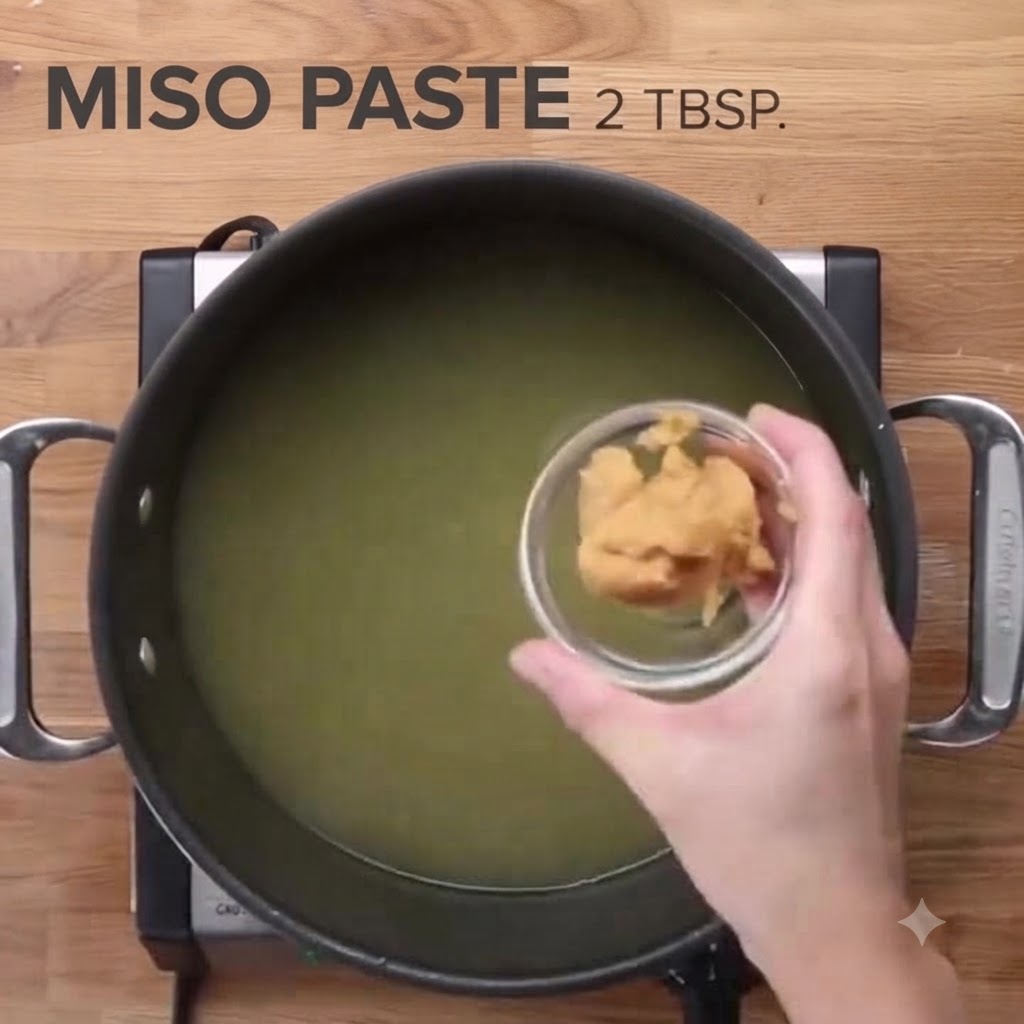 De la pâte miso versée dans une grande marmite de bouillon de poulet.